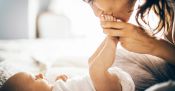 Woman kissing feet of baby laying on bed