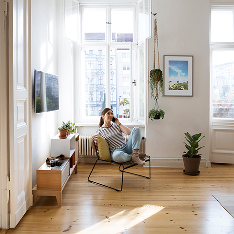 A person relaxing in a chair in a bright, modern living room with large windows, plants, and minimalist furniture.